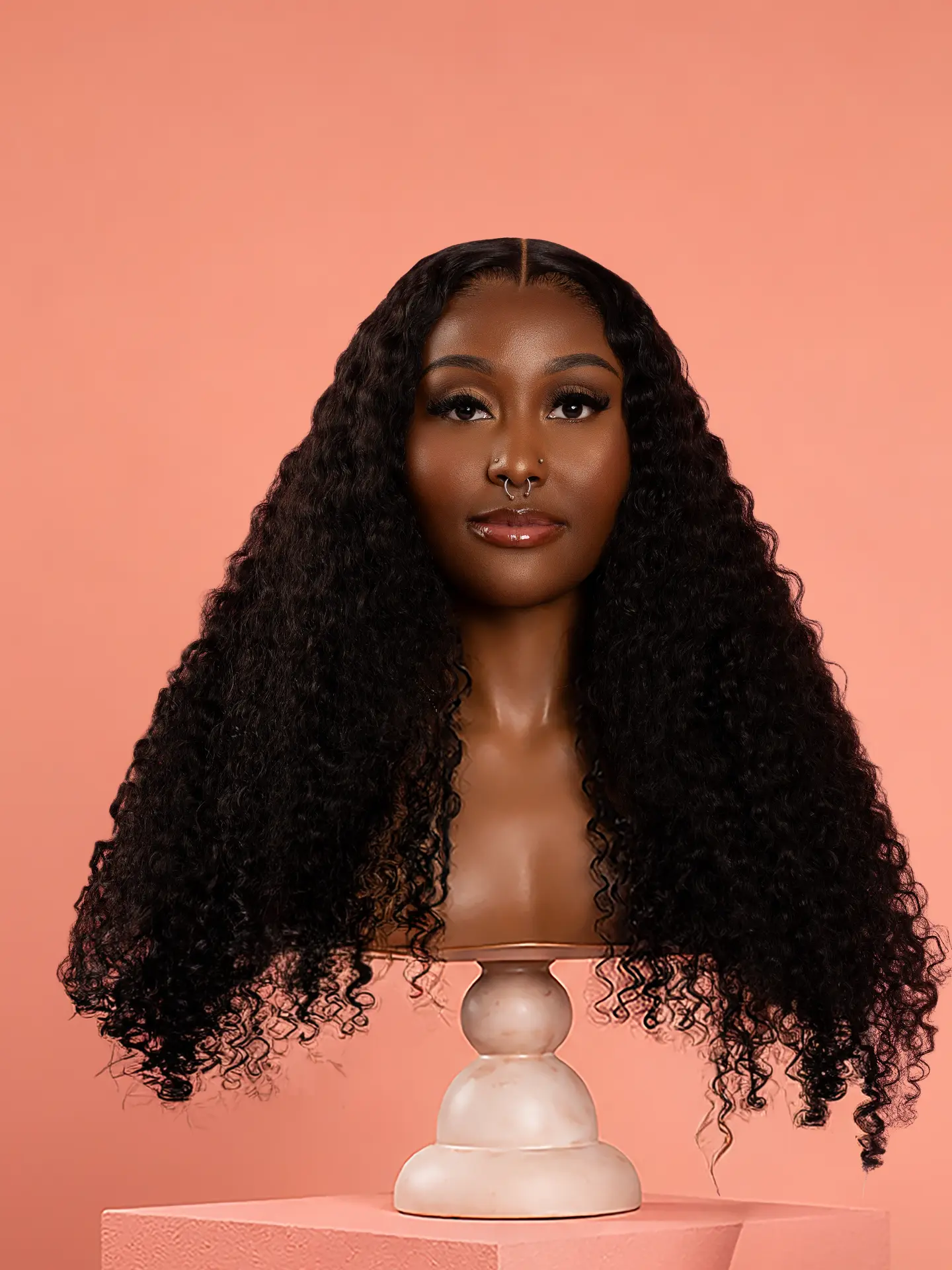 It Curl — Burmese Curly luxury wig on mannequin against a salmon pink backdrop